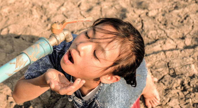 “Child trying to drink from a dry water tap in a cracked, drought-affected area, symbolizing the global challenge of water scarcity and limited accessibility